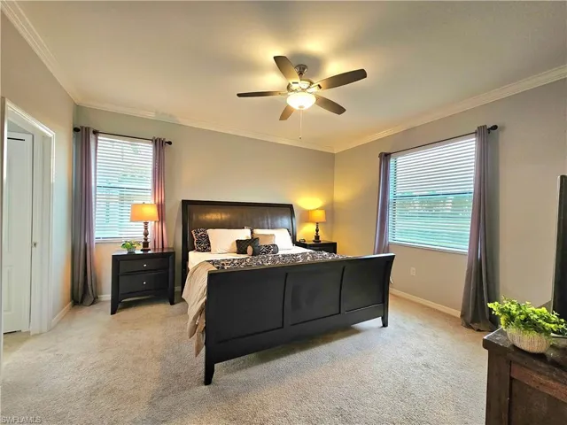 Bedroom with ceiling fan, light carpet, and ornamental molding