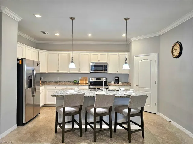 Kitchen featuring pendant lighting, a center island with sink, white cabinetry, and stainless steel appliances