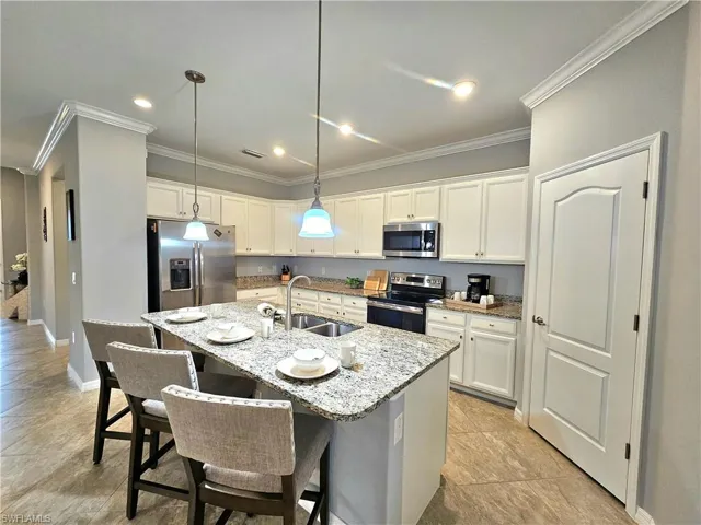 Kitchen featuring light stone counters, sink, stainless steel appliances, and an island with sink