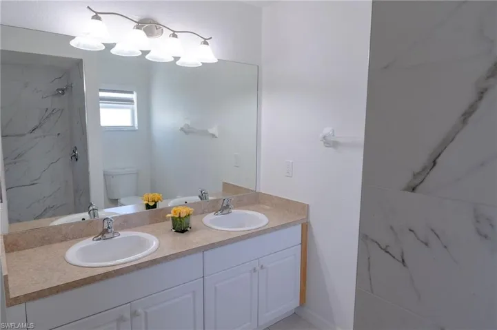 Full bath with double vanity and a marble finish shower