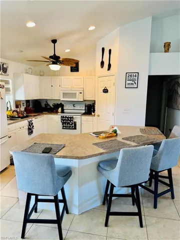Kitchen featuring a kitchen bar, white appliances, lofted ceiling, white cabinetry, and a center island