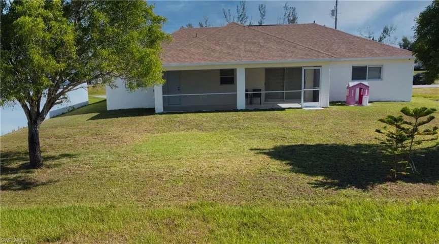 Rear view of house featuring a lawn, stucco siding, a shingled roof, and a sunroom