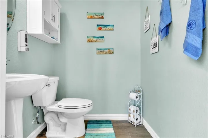 Pedestal sink with a white toilet, wall-mounted white cabinetry, and wood-finish flooring
