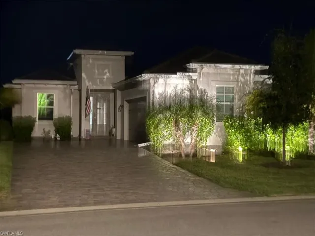 Contemporary stucco exterior with a paver driveway, integrated garage, and landscaped front yard featuring mature plantings