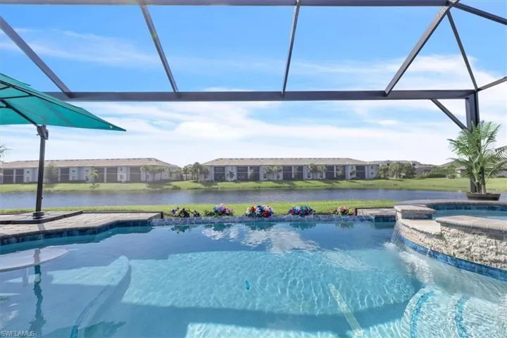 Screened enclosure encompassing a swimming pool with integrated spa and water feature, featuring a paved pool deck and water frontage