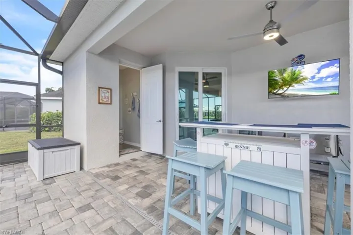 Screened-in outdoor patio featuring a patterned paver floor, built-in bar, and a ceiling fan with integrated lighting