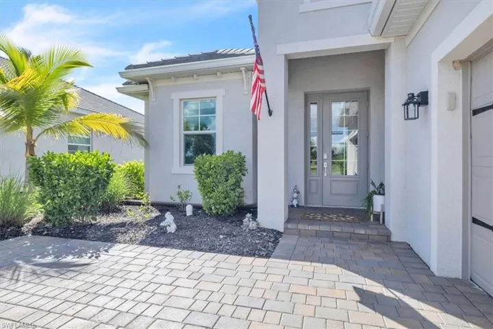 Paver driveway leading to a covered entry with double glass-panel doors