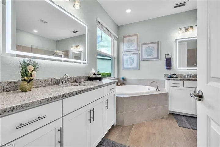 Dual vanity with white cabinetry, light-toned countertops, and illuminated mirrors
