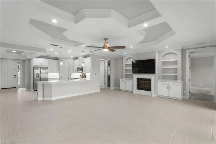 Unfurnished living room featuring crown molding, a sink, coffered ceiling, a glass covered fireplace, and a ceiling fan