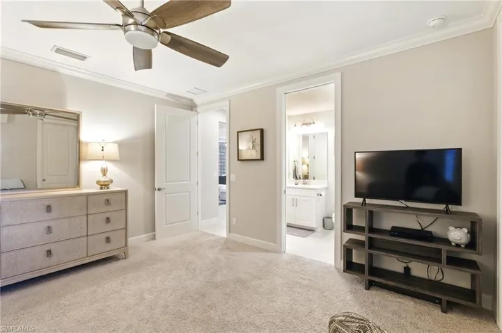 Carpeted bedroom with baseboards, ensuite bathroom, visible vents, and crown molding