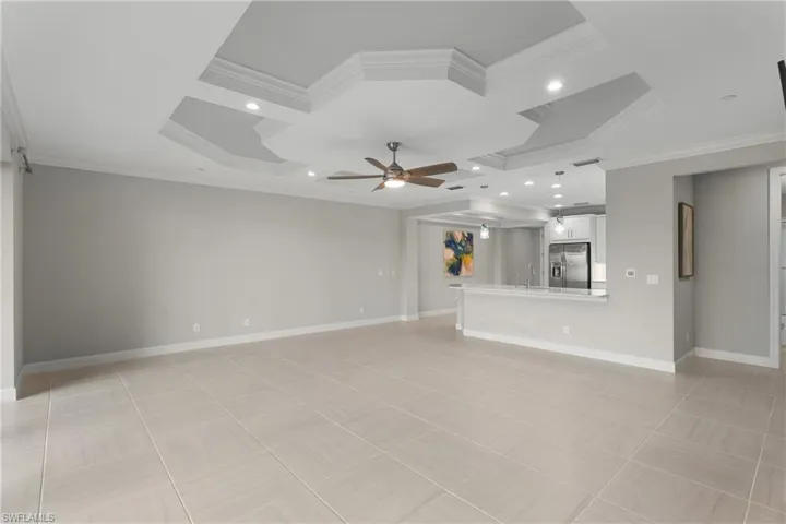 Unfurnished living room featuring crown molding, coffered ceiling, ceiling fan, baseboards, and a sink