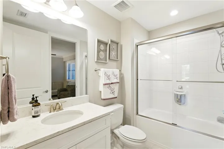 Bathroom featuring visible vents, shower / bath combination with glass door, toilet, and vanity