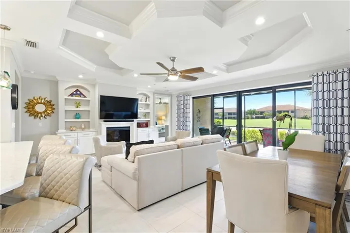 Living room with crown molding, coffered ceiling, built in shelves, visible vents, and a ceiling fan