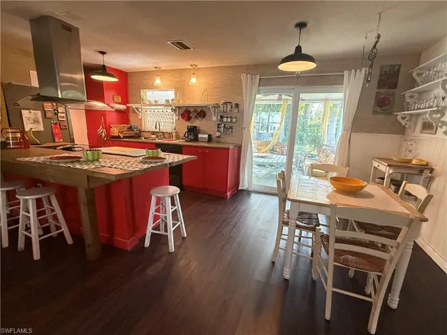 Kitchen featuring island exhaust hood, dark wood-style floors, wainscoting, a kitchen breakfast bar, and a sink