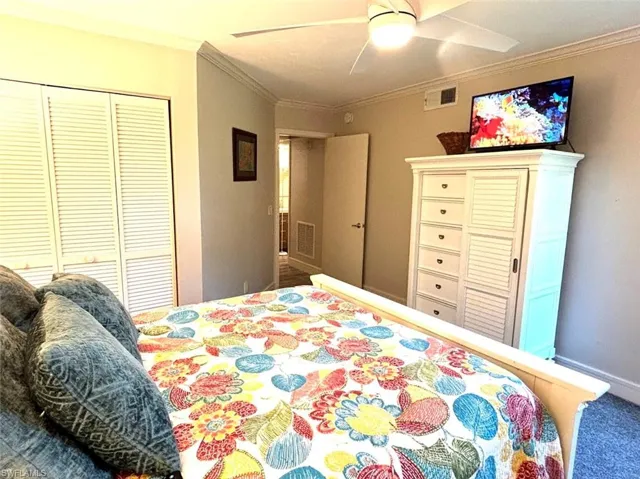 Bedroom featuring a ceiling fan, ornamental molding, carpet, and a closet