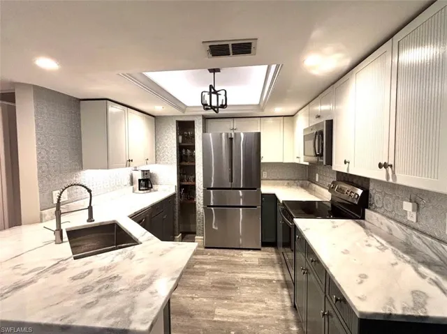 Kitchen with stainless steel appliances, light wood-type flooring, light stone countertops, a peninsula, and a tray ceiling