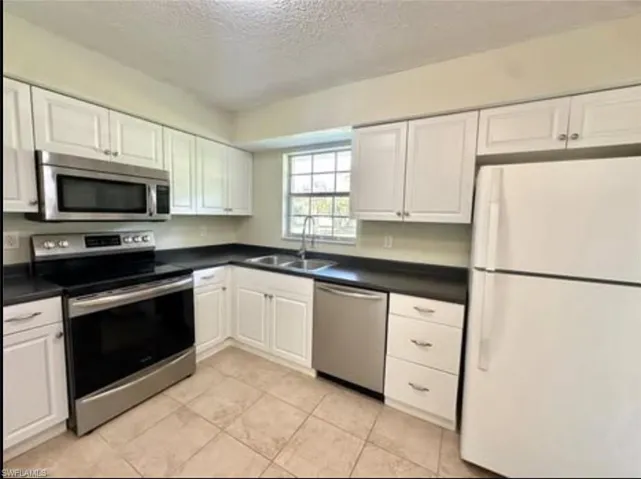 Kitchen featuring appliances with stainless steel finishes, a textured ceiling, white cabinetry, dark countertops, and light tile patterned floors