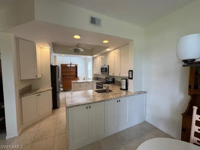 Kitchen featuring a peninsula, light stone countertops, stainless steel appliances, white cabinets, and ceiling fan