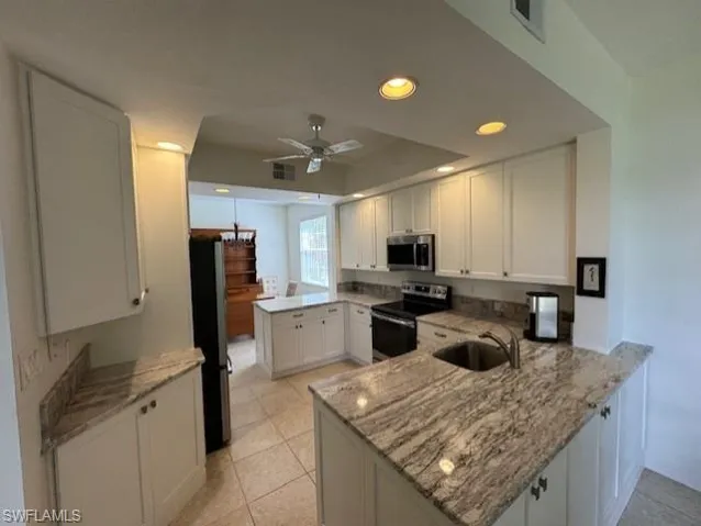 Kitchen featuring a peninsula, stainless steel appliances, white cabinetry, light stone counters, and recessed lighting