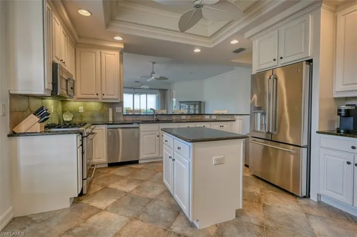 Kitchen with a center island, sink, a tray ceiling, appliances with stainless steel finishes, and white cabinets