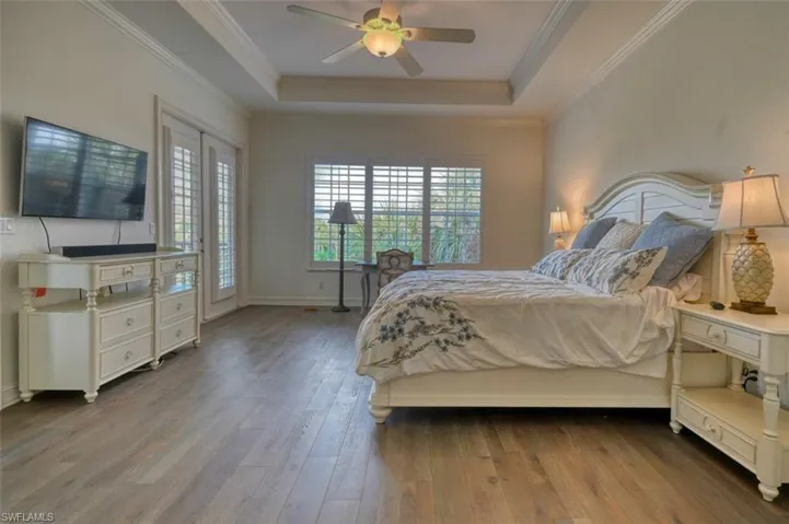 Bedroom featuring ceiling fan, light wood-type flooring, and a tray ceiling