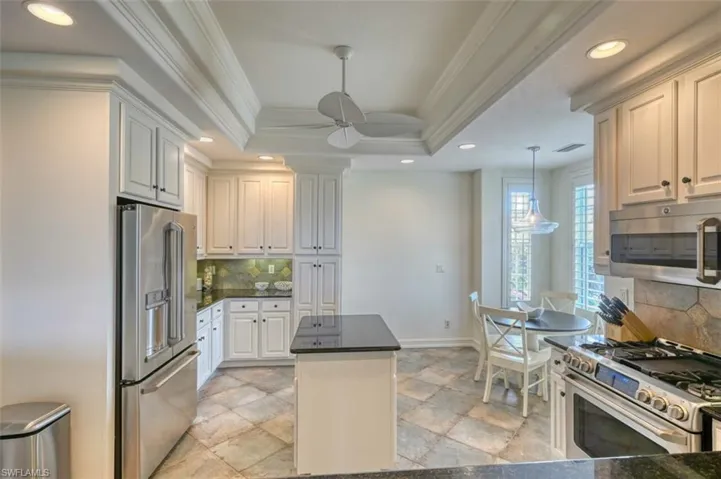 Kitchen with white cabinets, appliances with stainless steel finishes, tasteful backsplash, a tray ceiling, and crown molding