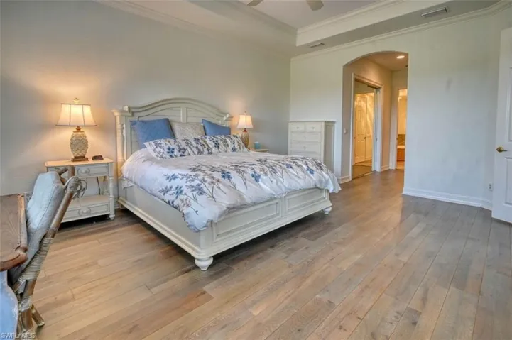Bedroom with ceiling fan, a raised ceiling, ornamental molding, and light wood-type flooring