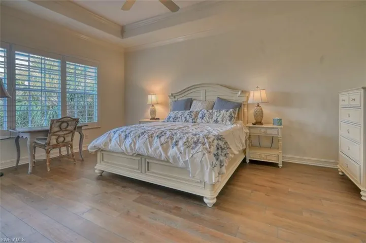 Bedroom featuring ceiling fan, light hardwood / wood-style flooring, a raised ceiling, and ornamental molding