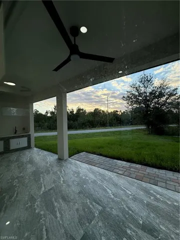 Patio terrace at dusk with a lawn, ceiling fan, and an outdoor kitchen
