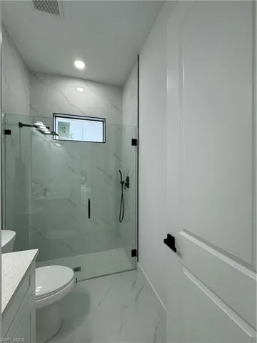 Bathroom featuring vanity, a shower with shower door, and toilet