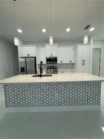 Kitchen featuring sink, hanging light fixtures, backsplash, white cabinets, and appliances with stainless steel finishes
