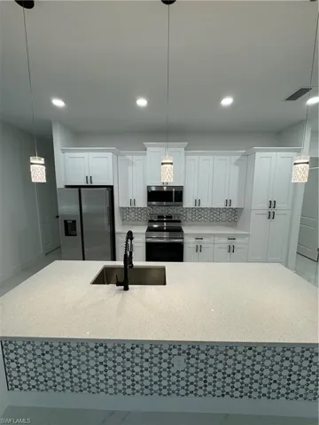Kitchen with hanging light fixtures, white cabinetry, sink, and appliances with stainless steel finishes
