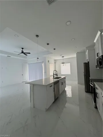 Kitchen with white cabinetry, dishwasher, pendant lighting, a center island with sink, and range