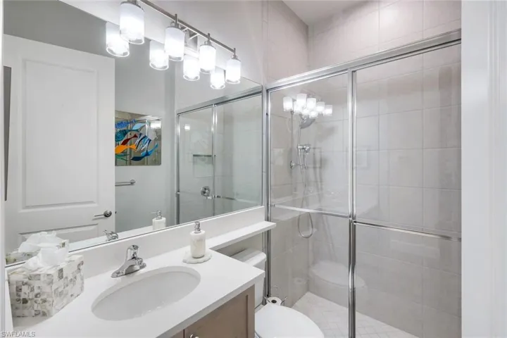 Guest bathroom features quartz countertop, tasteful vanity light fixture, walk-in shower with floor to ceiling tile.