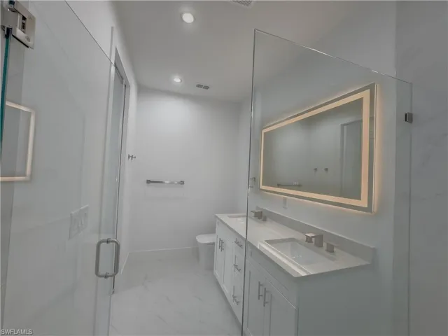 Full bathroom featuring double vanity, recessed lighting, light marble finish flooring, and a marble finish shower