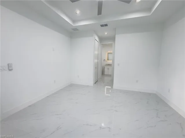 Unfurnished bedroom featuring a raised ceiling, light marble finish floors, recessed lighting, ceiling fan, and connected bathroom