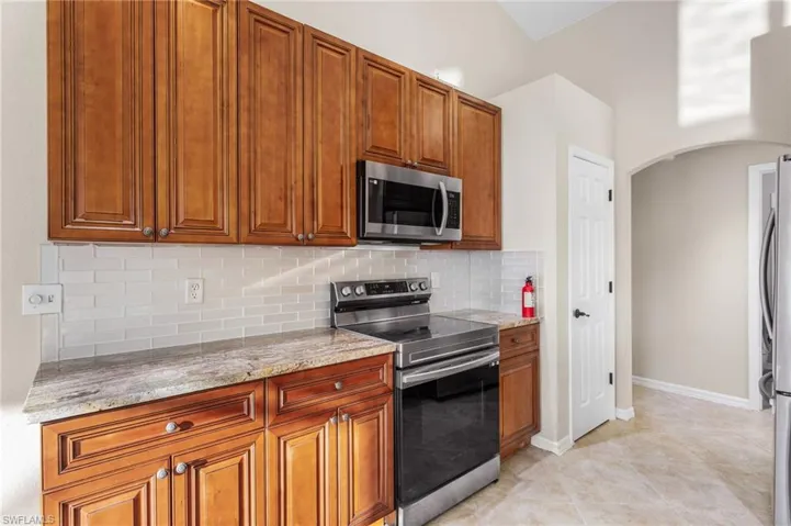 Kitchen with stainless steel appliances, arched walkways, decorative backsplash, light stone countertops, and wood finish cabinets