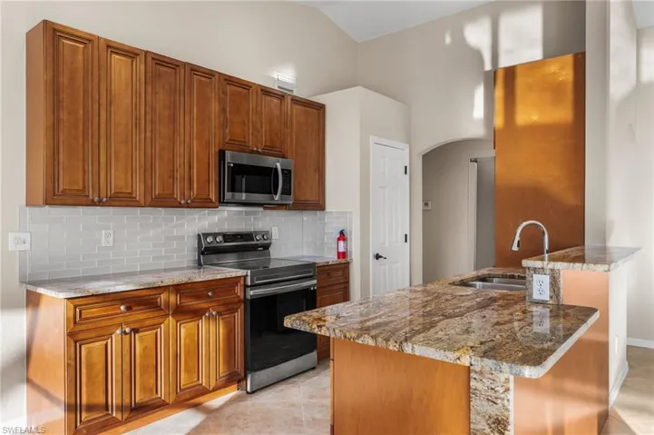 Kitchen with stainless steel appliances, light stone counters, wood finish cabinetry, arched walkways, and tasteful backsplash