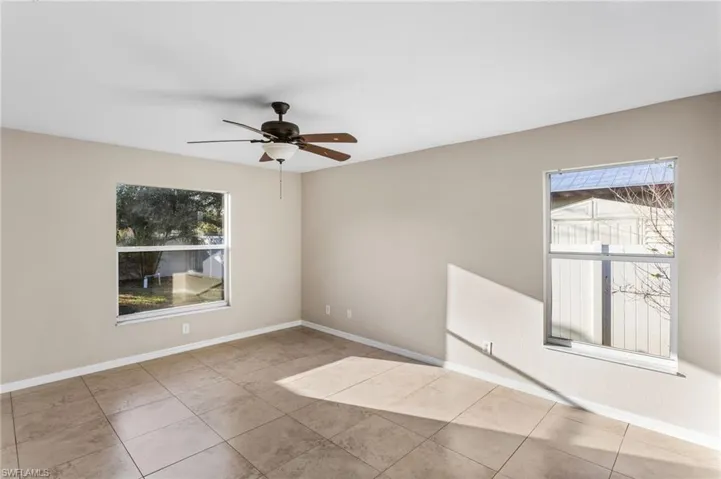 Tiled empty room featuring ceiling fan and baseboards