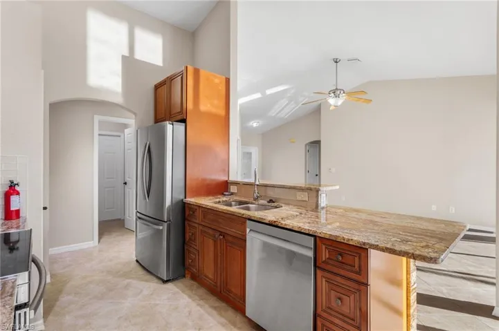 Kitchen featuring arched walkways, stainless steel appliances, wood finish cabinetry, light stone counters, and ceiling fan