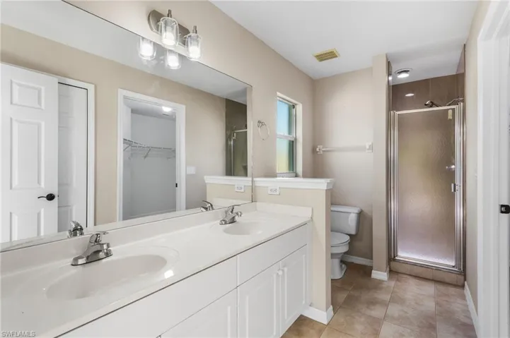 Bathroom with a spacious closet, a stall shower, double vanity, and light tile patterned flooring