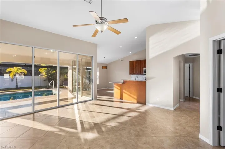 6 slider panels let in natural light. Arched hallway to primary suite, a ceiling fan in center of living room, recessed lighting, vaulted ceiling, and tile floors.