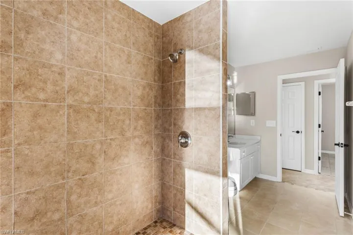 Full bath featuring tiled walk in shower, vanity, and light tile patterned floors