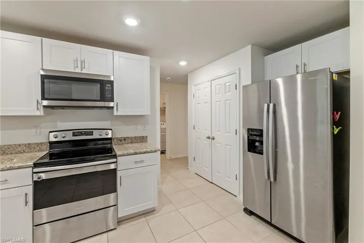 Kitchen featuring appliances with stainless steel finishes, white cabinetry, light tile patterned floors, light stone counters, and recessed lighting