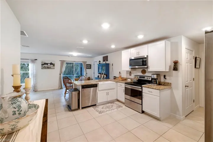Kitchen with a peninsula, stainless steel appliances, white cabinets, light tile patterned floors, and light stone counters