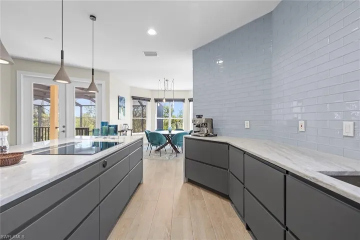 Contemporary kitchen featuring a large island with an induction cooktop, modern pendant lighting, and light wood-finish flooring