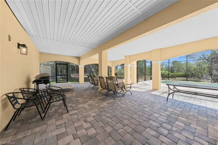 Spacious covered patio featuring multi-toned paver flooring, a white paneled ceiling, and arched openings