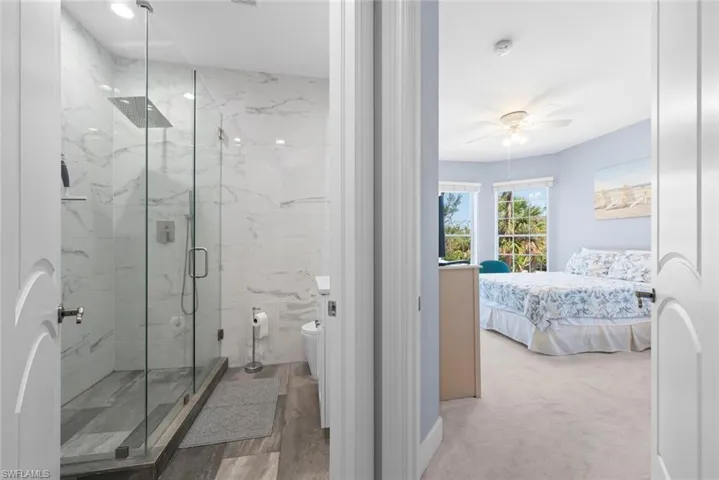 Spacious bathroom featuring a glass-enclosed shower with a rainfall showerhead, large format marble-look tile, and wood-finish flooring