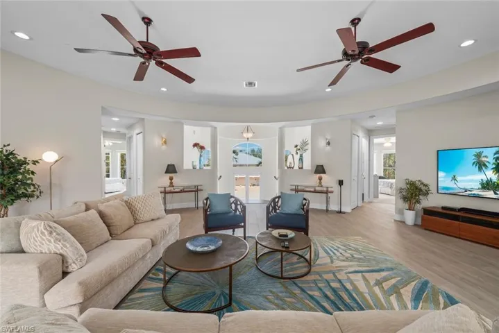 Spacious living area featuring light wood-finish flooring, two ceiling fans, recessed lighting, and curved architectural walls