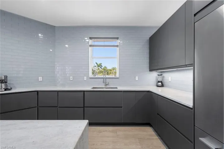Modern kitchen featuring dark flat-panel cabinetry, light stone countertops, and a full-height light blue subway tile backsplash